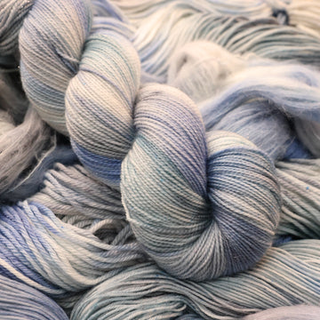 Sparkle yarn colored white that has very light blue and violet colors mixed in, on top of that same unwound yarn in differed weights.