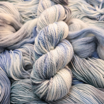 Bulky yarn colored white that has very light blue and violet colors mixed in, on top of that same unwound yarn in differed weights.