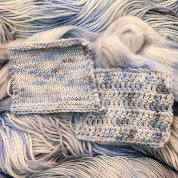 Crochet and Knit swatches colored white that has very light blue and violet colors mixed in, on top of that same unwound yarn in differed weights.