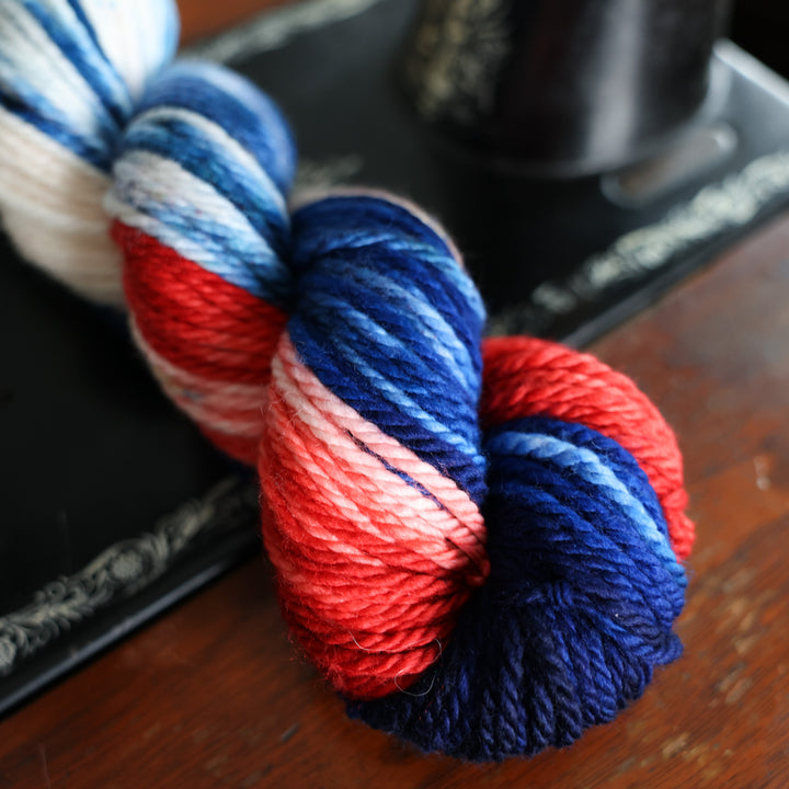 Bulky red white and blue yarn skeins on top of an old fashioned sewing table.