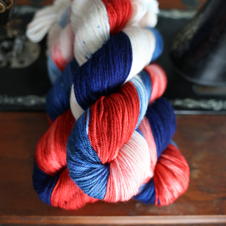 DK red white and blue yarn skeins on top of an old fashioned sewing table.