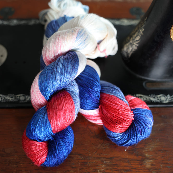 Silk DK red white and blue yarn skeins on top of an old fashioned sewing table.