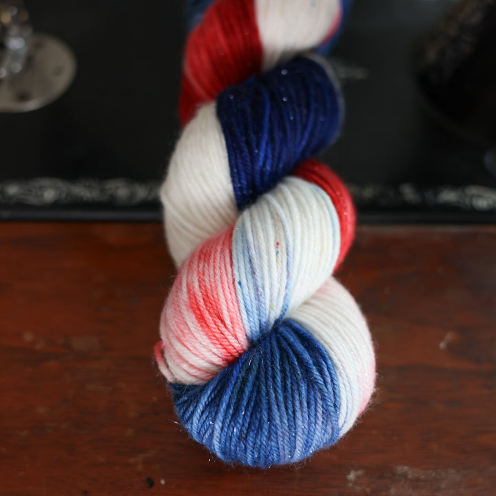 Sparkle DK red white and blue yarn skeins on top of an old fashioned sewing table.