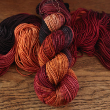 a sunset orange, red and dark purple worsted yarn with an unwound version on top of a light brown table.