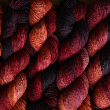 a sunset orange, red and dark purple yarn stacked neatly next to each other.