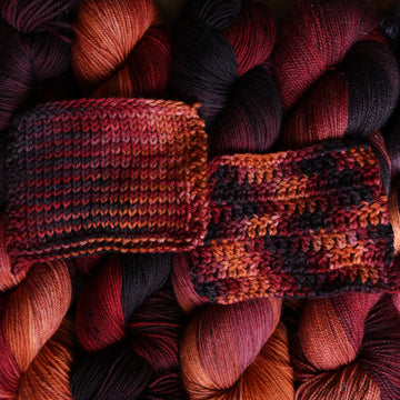a sunset orange, red and dark purple knit and crochet swatches on top of the same wound up yarn that is stacked neatly next to each other.