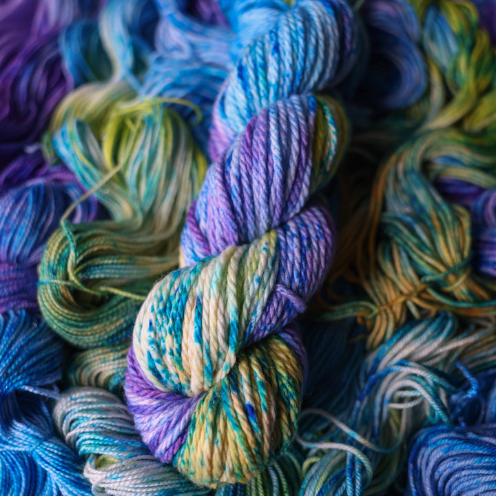 Bulky yarn colored different shades of light and dark blue along with purple and some yellows and orange and some green. This is on top of unwound skeins of this same color way.