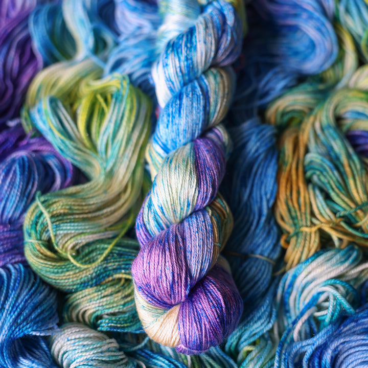 Silk yarn colored different shades of light and dark blue along with purple and some yellows and orange and some green. This is on top of unwound skeins of this same color way.