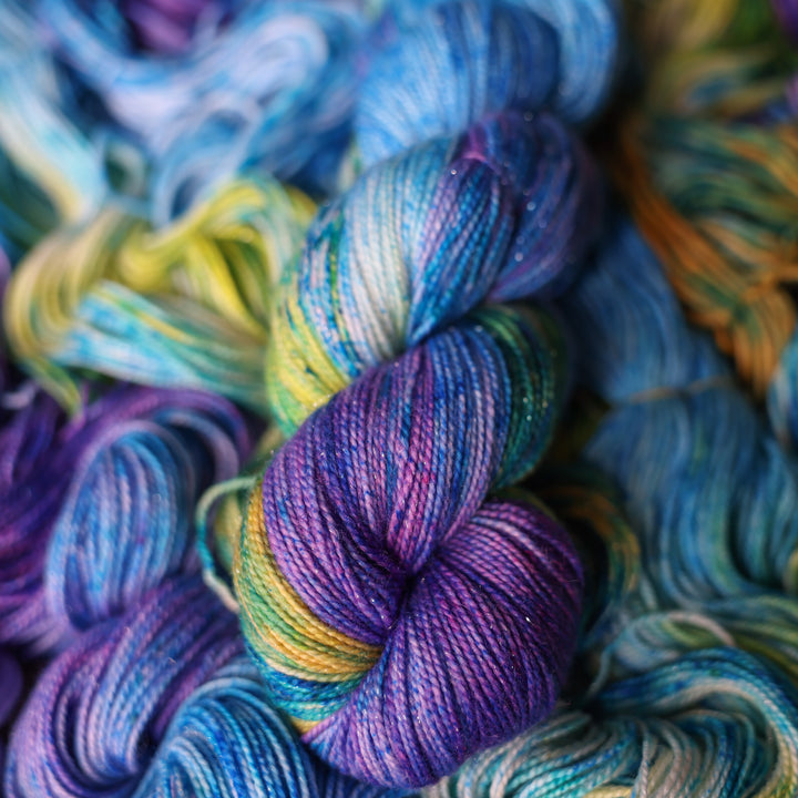 Sparkle yarn colored different shades of light and dark blue along with purple and some yellows and orange and some green. This is on top of unwound skeins of this same color way.