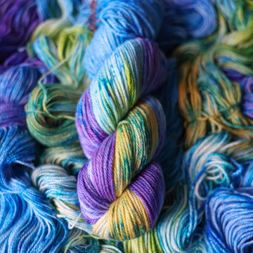 Worsted yarn colored different shades of light and dark blue along with purple and some yellows and orange and some green. This is on top of unwound skeins of this same color way.