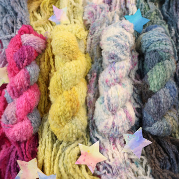 4 different colored fluffy bulky yarn skeins next to each other with the same an unwound version of each skein underneath their matching skein, with a couple of multicolored stars next to it.