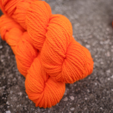 A couple of vibrant orange Bulky yarn skeins on top of gravel.