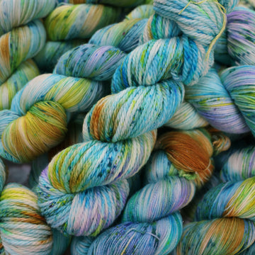 Bulky yarn with light shades of blue and speckles of purple, with some light greens and browns. There are more skeins like this of different weights underneath.
