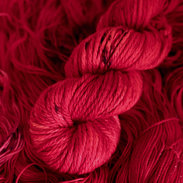 A vibrant red colored Bulky yarn with some dark speckles, on top of an unwound version of that same yarn.