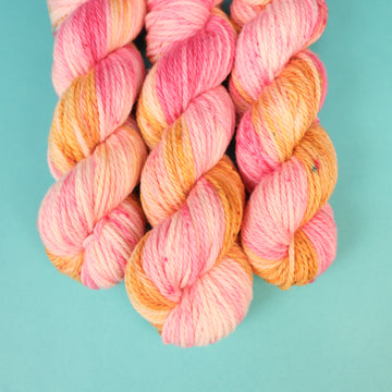 A couple of Bulky yarn skeins that are colored with a light pink, yellow, and orang e, on top of a light blue background.