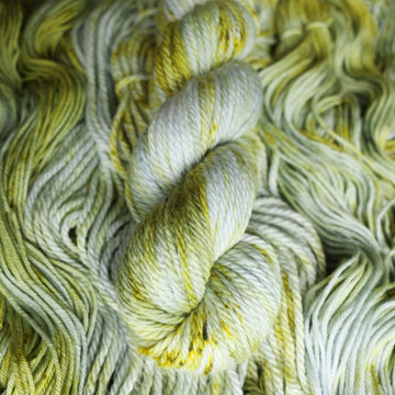 Bulky yarn colored with different shades of light green and white with some dark green speckles on top of the same unwound yarn.