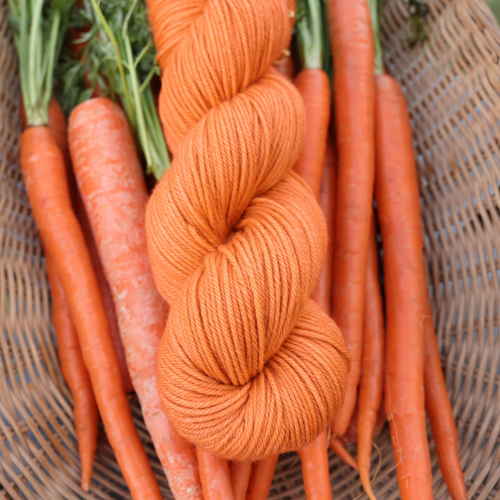 DK yarn colored a carrot orange color. This skin is on top of a basket of fresh garden carrots