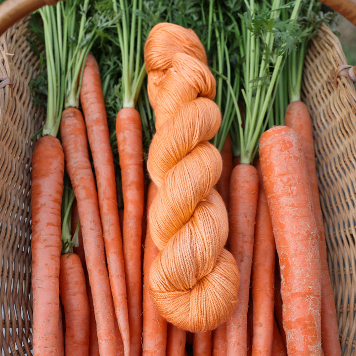 Silk yarn colored a carrot orange color. This skin is on top of a basket of fresh garden carrots