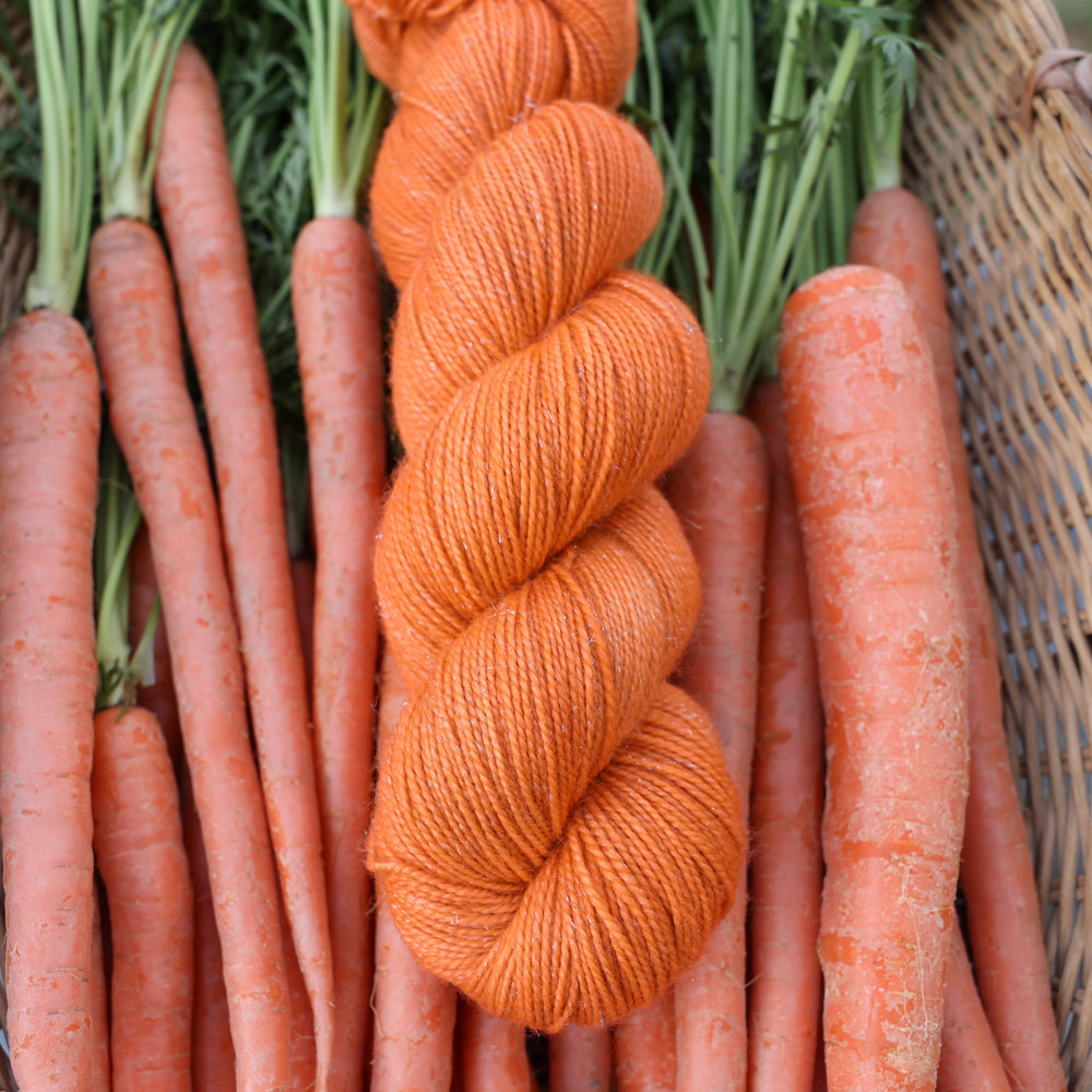 Fingering sparkle yarn colored a carrot orange color. This skin is on top of a basket of fresh garden carrots