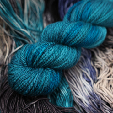 a dark ocean navy blue bulky yarn on top of unwound black white and blue yarn.