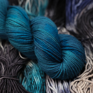 a dark ocean navy blue DK yarn on top of unwound black white and blue yarn.