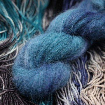 a dark ocean navy blue sport suri alpaca on top of unwound black white and blue yarn.