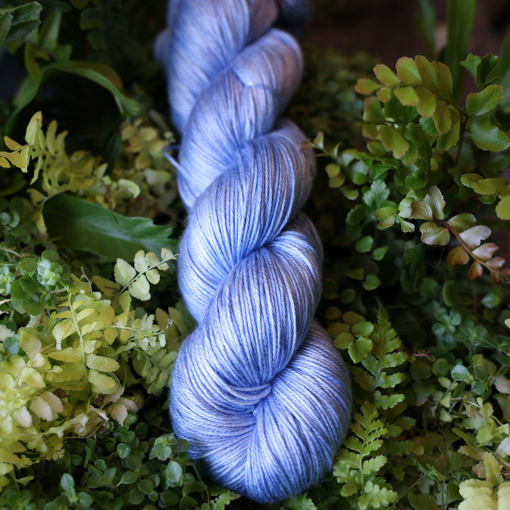 Silk yarn colored a light blue. This skein is on top of a bed of ferns and plants.