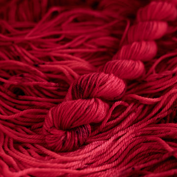 A vibrant red colored DK mini yarn with some dark speckles, on top of an unwound version of that same yarn.