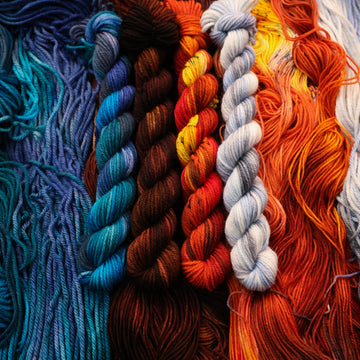 Blue, brown, red, and a light blue/white DK mini  yarn skeins with unwound skeins of each of those colors underneath its corresponding skein.