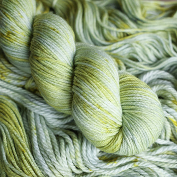 DK yarn colored with different shades of light green and white with some dark green speckles on top of the same unwound yarn.