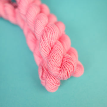 A light pink colored DK mini yarn on top of a light blue background.