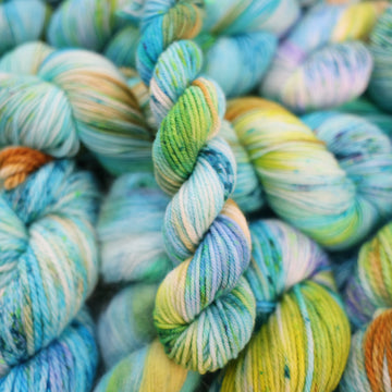 DK mini yarn with light shades of blue and speckles of purple, with some light greens and browns. There are more skeins like this of different weights underneath.