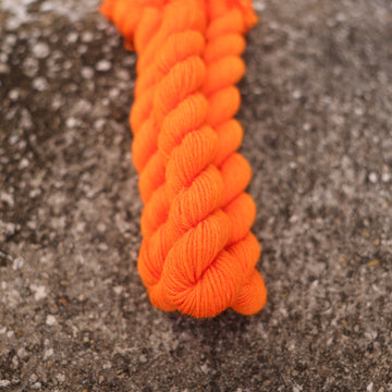 A couple of vibrant orange DK mini yarn skeins on top of gravel.