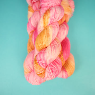 A couple of DK yarn skeins that are colored with a light pink, yellow, and orang e, on top of a light blue background.