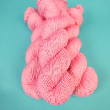 A light pink colored DK yarn on top of a light blue background.