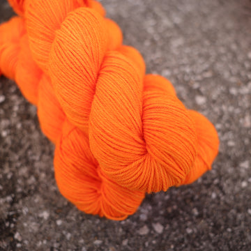 A couple of vibrant orange DK yarn skeins on top of gravel.