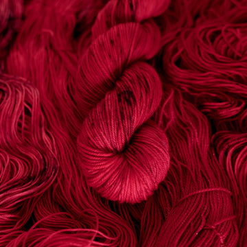 A vibrant red colored DK yarn with some dark speckles, on top of an unwound version of that same yarn.