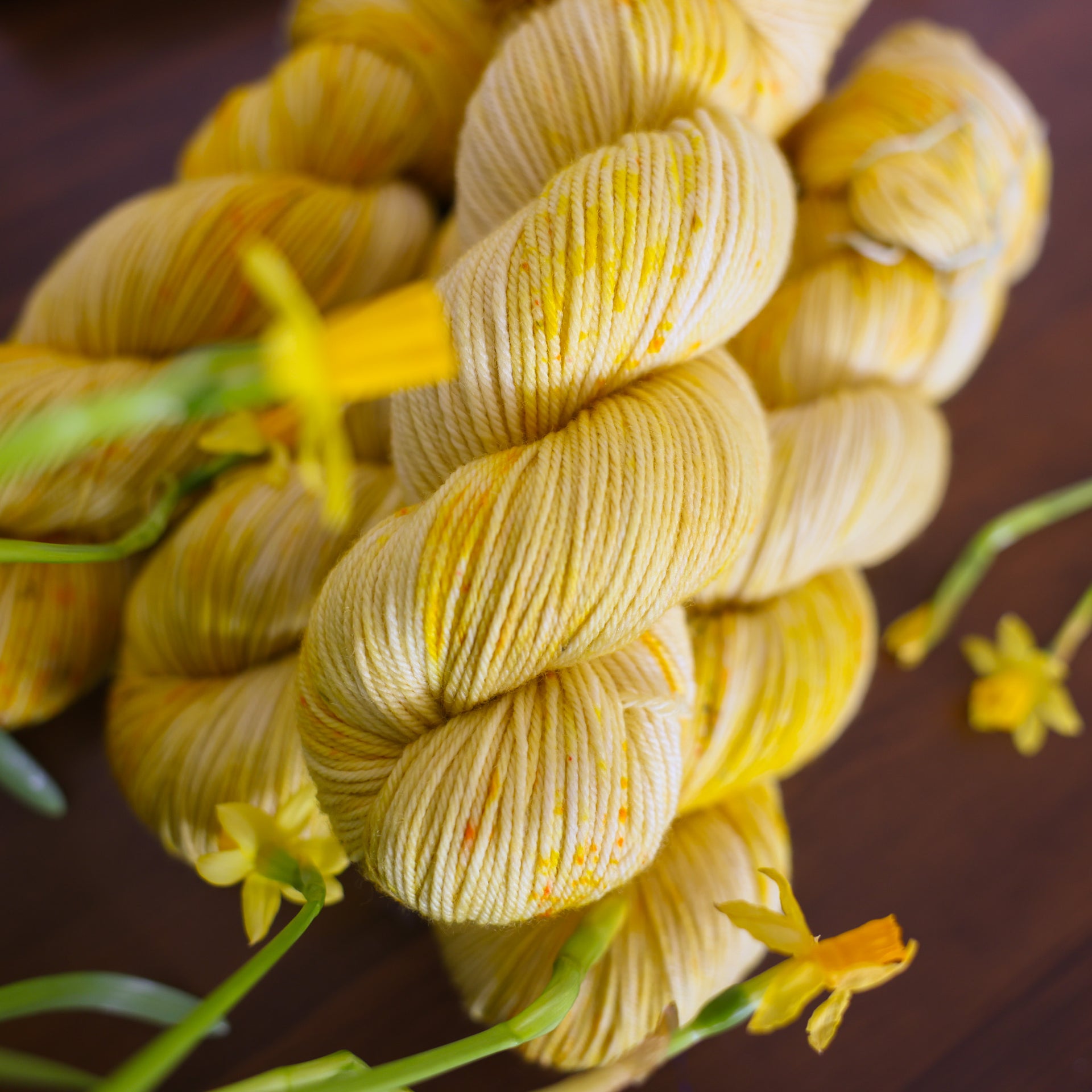 Four yellow varied DK yarn skeins sitting on top of a brown table surrounded by yellow flowers.