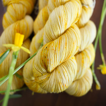 Four yellow varied sports skein sitting on top of a brown table surrounded by yellow flowers.