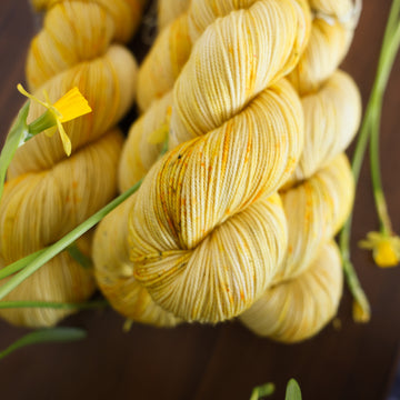Four yellow varied sports skein sitting on top of a brown table surrounded by yellow flowers.