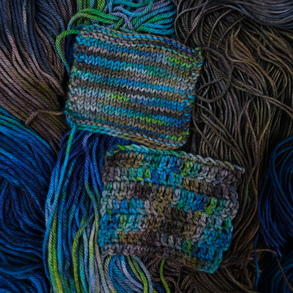 Crochet and knit swatches colored with dark brown dark blue and green. This is all on top of unwound skeins of this same color way.