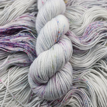 DK yarn colored a light grey with some pink, purple, and blue speckles. This skein is on top of unwound yarn of the same color way.