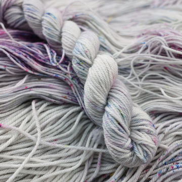 DK mini yarn colored a light grey with some pink, purple, and blue speckles. This skein is on top of unwound yarn of the same color way.