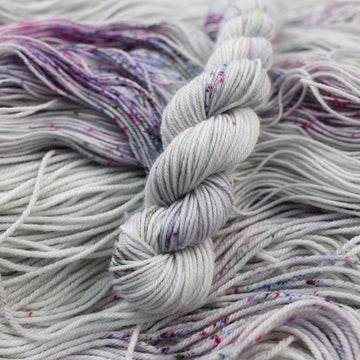 Fingering mini yarn colored a light grey with some pink, purple, and blue speckles. This skein is on top of unwound yarn of the same color way.