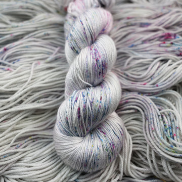 Silk yarn colored a light grey with some pink, purple, and blue speckles. This skein is on top of unwound yarn of the same color way.