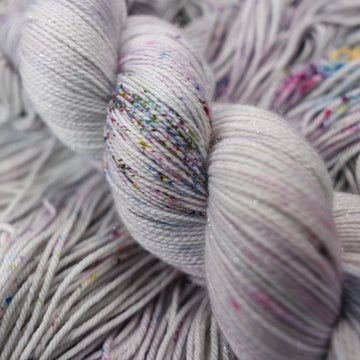 Sparkle yarn colored a light grey with some pink, purple, and blue speckles. This skein is on top of unwound yarn of the same color way.