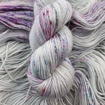 Worsted yarn colored a light grey with some pink, purple, and blue speckles. This skein is on top of unwound yarn of the same color way.