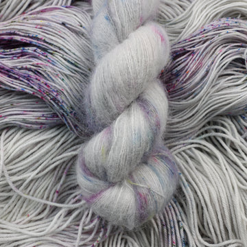 Suri yarn colored a light grey with some pink, purple, and blue speckles. This skein is on top of unwound yarn of the same color way.