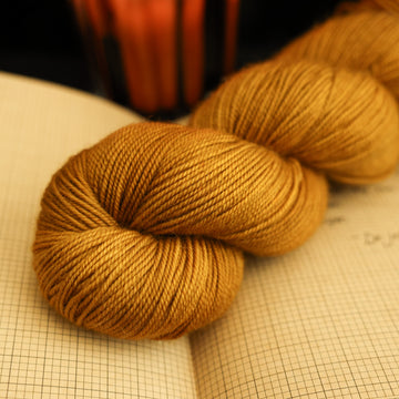 A light burnt orange sport yarn on top of an open notebook with a lit orange candle in the back, all on a black background