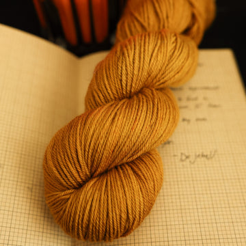 A light burnt orange DK yarn on top of an open notebook that has a letter written on it and a lit orange candle in the back, all on a black background
